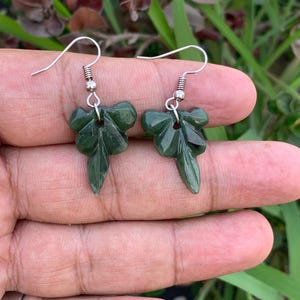 Puede incluir: Un par de pendientes de hoja verde con ganchos de plata. Los pendientes están tallados en jade y tienen un diseño detallado.