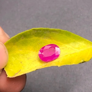 May include: A vibrant pink oval-shaped gemstone on a yellow leaf.
