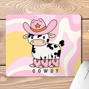 Könnte beinhalten: Ein rosa und gelbes Mauspad mit einer Comic-Kuh, die einen rosa Cowboyhut und Stiefel trägt. Der Text "COWDY" ist unter der Kuh gedruckt.
