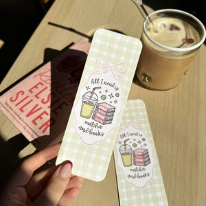 Op de afbeelding: Twee bladwijzers met de tekst "All I need is matcha and books" en een illustratie van matcha-drank en boeken. De bladwijzers hebben een lichtgroen ruitpatroon en een roze strikdesign. Op de achtergrond een boek met de titel "Elsie Silver".