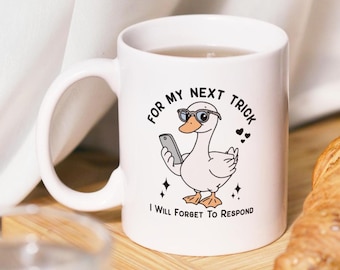 May include: White ceramic mug with a humorous graphic of a duck wearing sunglasses and holding a phone. The text reads "For my next trick I will forget to respond."
