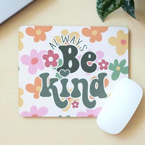 Peut inclure: Tapis de souris rectangulaire avec un motif floral dans les tons orange, rose et jaune. Les mots "Always Be Kind" sont imprimés dans une police rétro. Une souris d'ordinateur blanche est à côté du tapis.