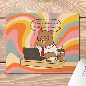 May include: A rectangular mouse mat featuring a cartoon bear wearing glasses and a red tie, working on a laptop. The mat has a retro swirl background in orange, pink, and yellow. Text reads, "I hope this email finds you before I do."