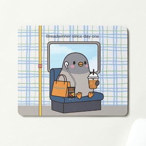 May include: A mouse mat with a cartoon pigeon on a bus. The pigeon has headphones, a drink, and a shopping bag. The text "Breadwinner since day one" is above the window. The background has a blue and white plaid pattern.
