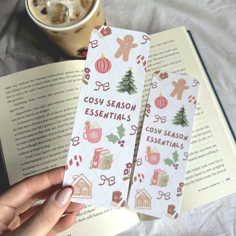 May include: Two rectangular bookmarks with a festive design. The bookmarks feature gingerbread men, Christmas trees, and the text "COSY SEASON ESSENTIALS." The background is a light cream color with a diamond pattern.