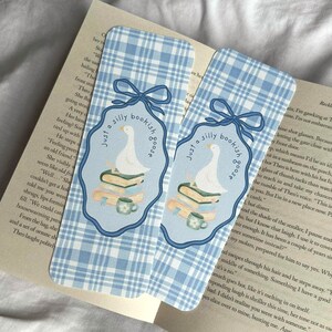 May include: Two blue and white plaid bookmarks with a whimsical design. Each bookmark features a cartoon goose on a stack of books, with the text "Just a silly bookish goose". A cute gift for book lovers.