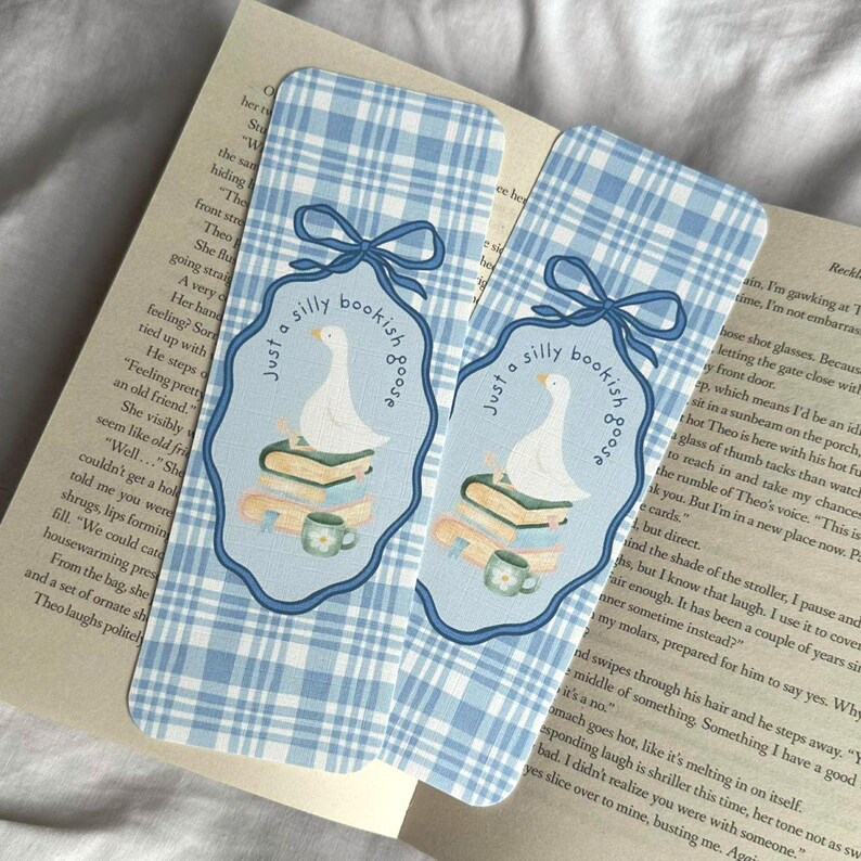 May include: Two blue and white plaid bookmarks with a whimsical design. Each bookmark features a cartoon goose on a stack of books, with the text "Just a silly bookish goose". A cute gift for book lovers.