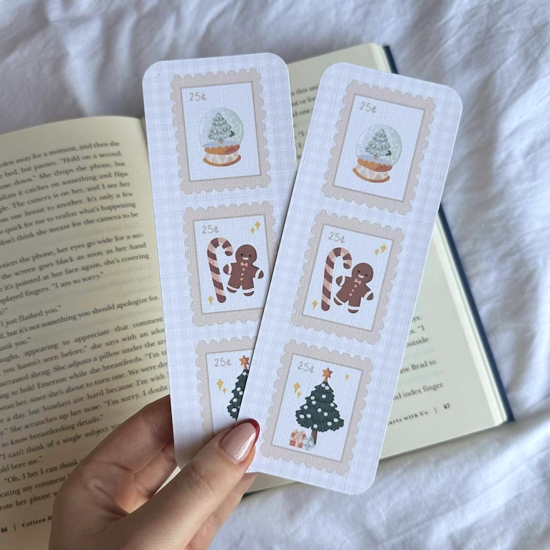 May include: Two festive bookmarks with a postage stamp design. Each bookmark features a snow globe, gingerbread man with a candy cane, and a Christmas tree. The bookmarks are light beige with a checkered pattern.