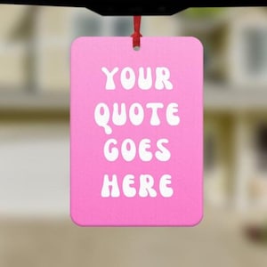 May include: A pink rectangular ornament with the text "YOUR QUOTE GOES HERE" in white, hanging from a red ribbon. The ornament is likely made of a sturdy material and is designed to be displayed.