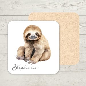 May include: Square coaster with a watercolour illustration of a sloth with light brown fur. The sloth is sitting and smiling. The name "Stephanie" is written in cursive below the sloth. A second, plain, tan coaster is behind the sloth coaster.