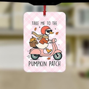 May include: Rectangular ornament with a pink and white plaid pattern. It depicts a cartoon duck on a pink scooter, carrying a pumpkin. The text on the ornament says "TAKE ME TO THE PUMPKIN PATCH."