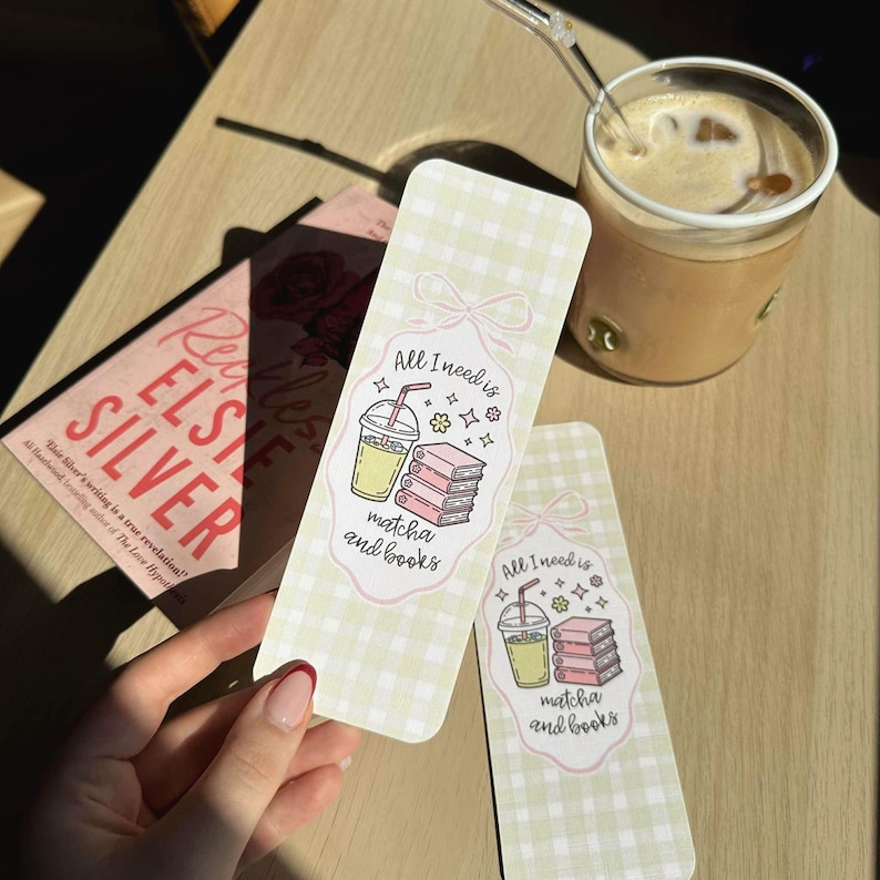 Op de afbeelding: Twee rechthoekige bladwijzers met een lichtgroen ruitpatroon. Elke bladwijzer heeft een cartoonillustratie van een matcha-drankje en boeken, met de tekst "All I need is matcha and books". Een boek met de titel "Reckless Elsie Silver" is ook zichtbaar.