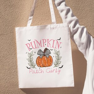 May include: White tote bag with a pumpkin design and the text "Pumpkin Patch Girly". The pumpkin is orange with a black and white checkered bow. Green leaves and black bats surround the pumpkin.