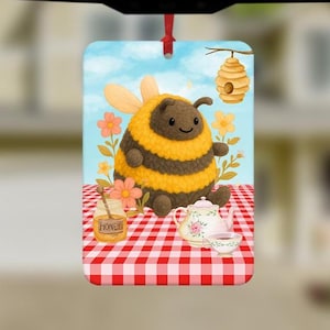 Può includere: Ornamento rettangolare con un'ape dei cartoni animati a strisce gialle e nere, seduta su una coperta da picnic a scacchi rossi e bianchi. Una teiera, una tazza da tè e un barattolo di miele sono anche sulla coperta. Un alveare è appeso a un ramo di un albero sullo sfondo.