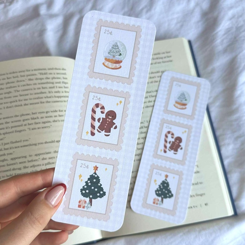 May include: Two Christmas-themed bookmarks with postage stamp designs. Each bookmark features three stamps with festive illustrations: a snow globe, a gingerbread man, and a Christmas tree. The stamps are framed in a light pink border, with the price 25p printed on each.