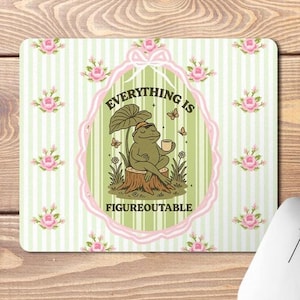 May include: A rectangular mouse mat with a green and white striped background and pink floral accents. The centre features a cartoon frog on a tree stump, holding a cup, with the text "EVERYTHING IS FIGUREOUTABLE".