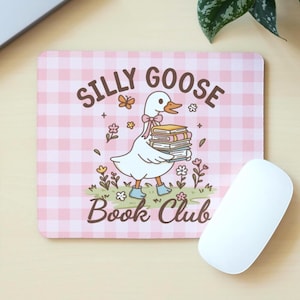 Könnte beinhalten: Rosa kariertes Mousepad mit der Aufschrift "Silly Goose Book Club" und einer Comic-Gans, die Bücher trägt. Die Gans ist weiß mit einer rosa Schleife und blauen Stiefeln. Eine weiße Computermaus liegt daneben.