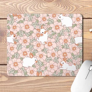 May include: A pink and white mouse mat with a floral pattern and white rabbits. The rabbits are in various poses, including sitting, standing, and hopping. The floral pattern is made up of pink and white flowers with green leaves.