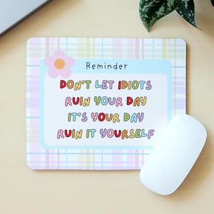 May include: A rectangular mouse mat with a pastel plaid pattern and a light blue box containing the text "DON'T LET IDIOTS RUIN YOUR DAY IT'S YOUR DAY RUIN IT YOURSELF". A white mouse is on the right.