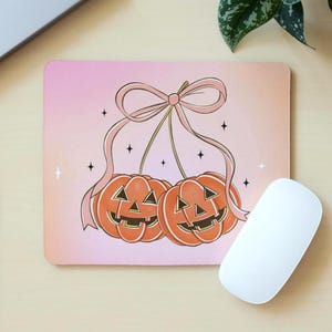 Może przedstawiać: Prostokątna podkładka pod mysz z motywem Halloween. Dwie pomarańczowe dynie połączone są różową wstążką, na tle różowego gradientu. Małe czarne gwiazdki i białe iskierki rozrzucone są wokół dyń.