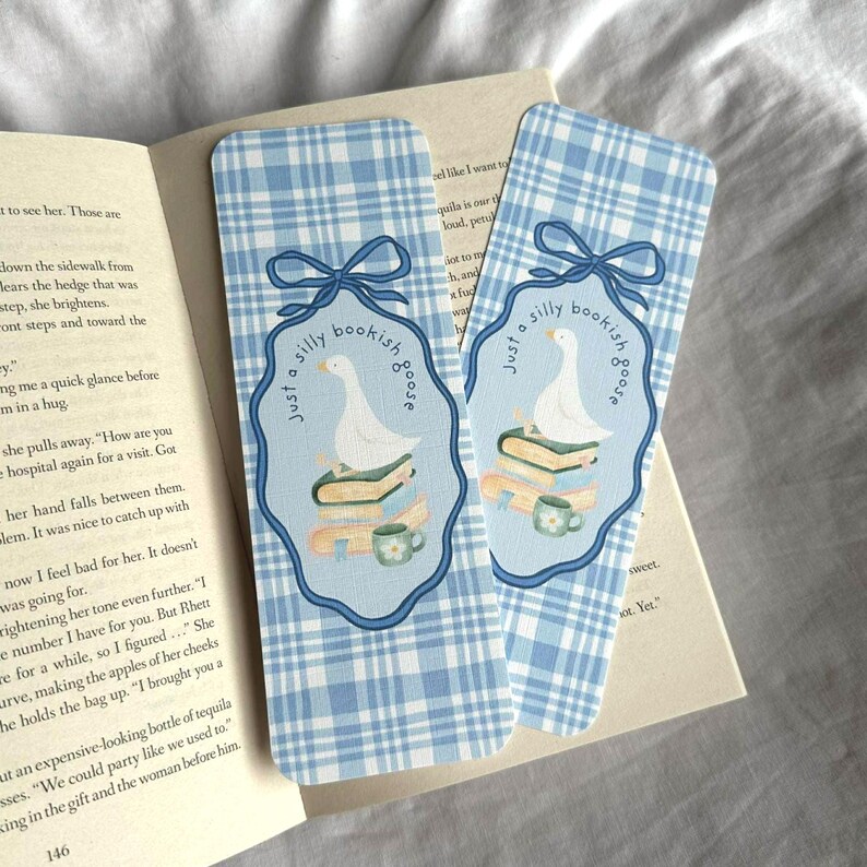 May include: Two blue and white plaid bookmarks with a whimsical design. Each bookmark features a light blue oval with a goose on books, a teacup, and the text "Just a silly bookish goose". A blue bow is at the top.