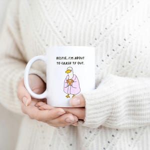 May include: White ceramic mug with a humorous illustration of a duck wearing a pink robe and holding a cup. The mug has the text "Bestie, I'm about to crash TF out." A fun, novelty item.
