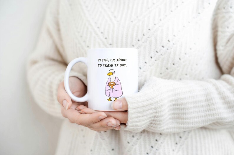 May include: White ceramic mug with a humorous illustration of a duck wearing a pink robe and holding a cup. The mug has the text "Bestie, I'm about to crash TF out." A fun, novelty item.