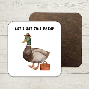 May include: A white coaster featuring the text "Let's get this bread" and a cartoon illustration of a duck wearing a brown hat and carrying a brown briefcase.