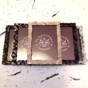 May include: Three picture frames made of natural stones. The frames are in shades of green, purple, and pink. The centre frame has a logo that says "The Aurora Palace" and "handmade".