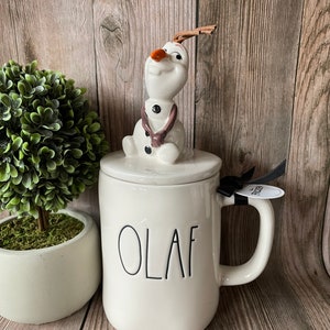 May include: White ceramic mug with a black "OLAF" inscription. The mug has a lid with a ceramic Olaf figurine from the movie Frozen.