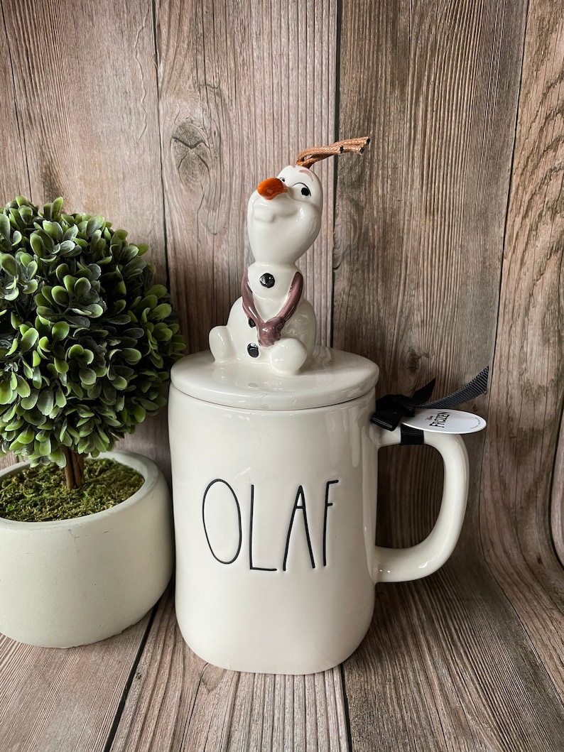 May include: White ceramic mug with a black "OLAF" inscription. The mug has a lid with a ceramic Olaf figurine from the movie Frozen.