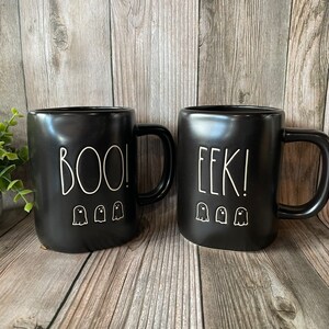 May include: Two black ceramic mugs with white ghost designs and the words "BOO!" and "EEK!" on them.