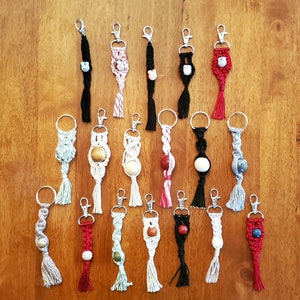 May include: A collection of 16 colorful macrame keychains with various beads and tassels. The keychains are made with different colored cords and feature a variety of bead styles.