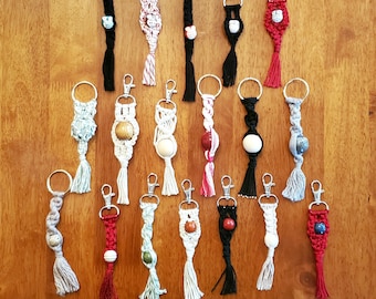 May include: A collection of 16 colorful macrame keychains with various beads and tassels. The keychains are made with different colored cords and feature a variety of bead styles.