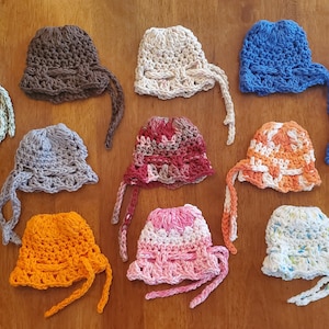 May include: A collection of 14 crocheted hats in various colors and patterns, including red, white, blue, green, brown, orange, and pink. The hats have a wide brim and a tie at the back.