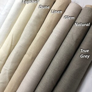 May include: Close-up of ten fabric rolls in various shades of beige, grey, and white. The rolls are labelled with the following names: White, Oyster, Eggshell, Dune, Linen, Glem, Natural, True Grey.