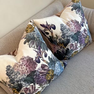 May include: Two decorative throw pillows with a floral pattern featuring purple, blue, and yellow flowers on a white background.
