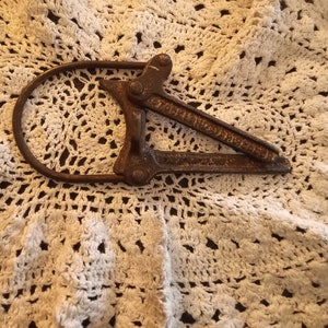 May include: A vintage metal bottle opener with a handle that forms a loop. The opener is rusty and has a worn finish.