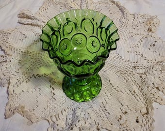 May include: A green glass pedestal bowl with a ruffled rim. The bowl features a star and moon design and sits on a round base. The bowl is approximately 6 inches in diameter and 5 inches tall.