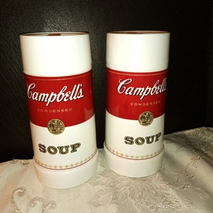 May include: Two white ceramic soup mugs with red and gold Campbell's Soup labels. The labels read "Campbell's Condensed Soup".
