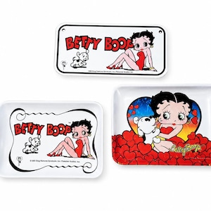 May include: Three rectangular trays featuring Betty Boop and her dog Pudgy. One tray is a sign with holes, while two are serving trays. The graphics show Betty Boop in a red dress with red hearts and the text BETTY BOOP in red lettering.