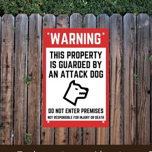 May include: Red and white warning sign with the text "WARNING" in bold, "THIS PROPERTY IS GUARDED BY AN ATTACK DOG" and "DO NOT ENTER PREMISES NOT RESPONSIBLE FOR INJURY OR DEATH". A black silhouette of a dog's head with a menacing expression is in the center of the sign. The sign is mounted on a wooden fence.