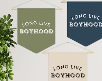 May include: Three wall banners with the text "Long Live Boyhood" in different colors and fonts. The banners are hanging on a white wall with a green plant in the corner.