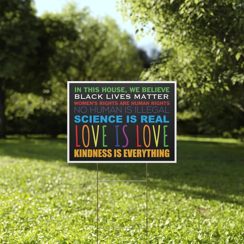 Puede incluir: Un letrero rectangular para jard&iacute;n con fondo negro y texto multicolor que dice: IN THIS HOUSE, WE BELIEVE, BLACK LIVES MATTER, WOMEN'S RIGHTS ARE HUMAN RIGHTS, NO HUMAN IS ILLEGAL, SCIENCE IS REAL, LOVE IS LOVE, KINDNESS IS EVERYTHING.