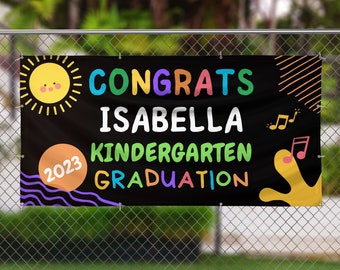 May include: Black banner with colorful text that reads "Congrats Isabella Kindergarten Graduation 2023". The banner has a sun, musical notes, and abstract shapes.