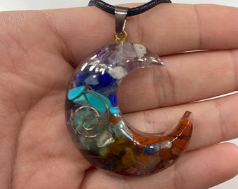 May include: Crescent moon pendant necklace with a variety of colorful gemstones and a copper wire spiral. The pendant is suspended from a black cord. The gemstones include blue, green, orange, and purple stones.