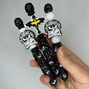 May include: Three black and silver pens with rhinestones and a dragon and book charm. The charms are white with black details and the text "In My Fantasy Era".