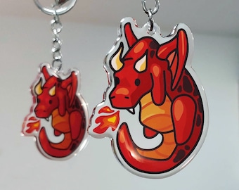 Puede incluir: Dos llaveros de dragón rojo con cadenas plateadas. El llavero más grande presenta un dragón con llamas saliendo de su boca. El llavero más pequeño presenta un dragón con una cola enroscada.