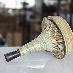 May include: A ceramic pipe with a bulbous head and a long, slender stem. The head features a brown and tan floral design with a dark brown rim. The stem is light green with a dark metal end.