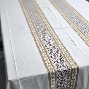 May include: A white tablecloth with two brown and beige patterned stripes running down the length of the fabric.
